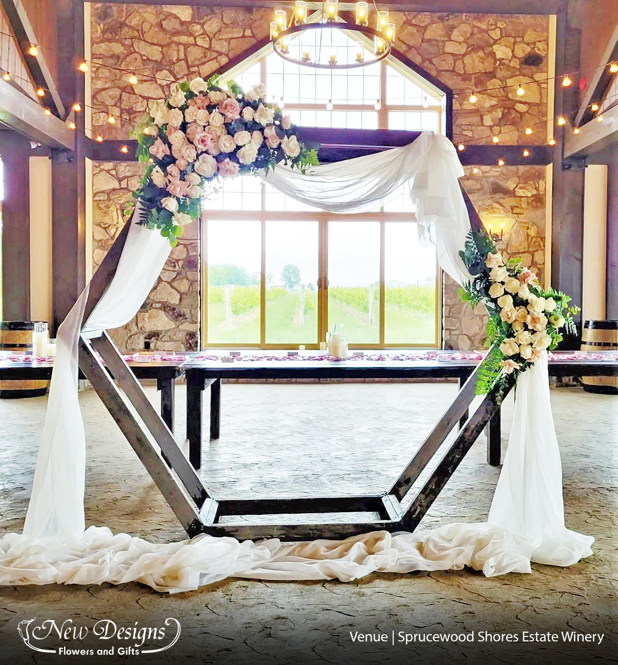 A Hexagon Wooden Arch in a Cobblestone Winery, with white draped chiffon, and white floral installments